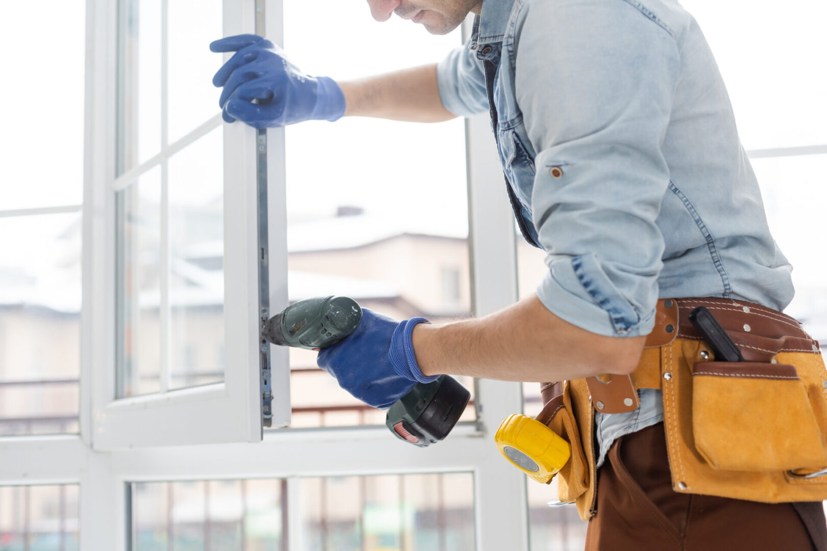 Worker installing window with power drill.